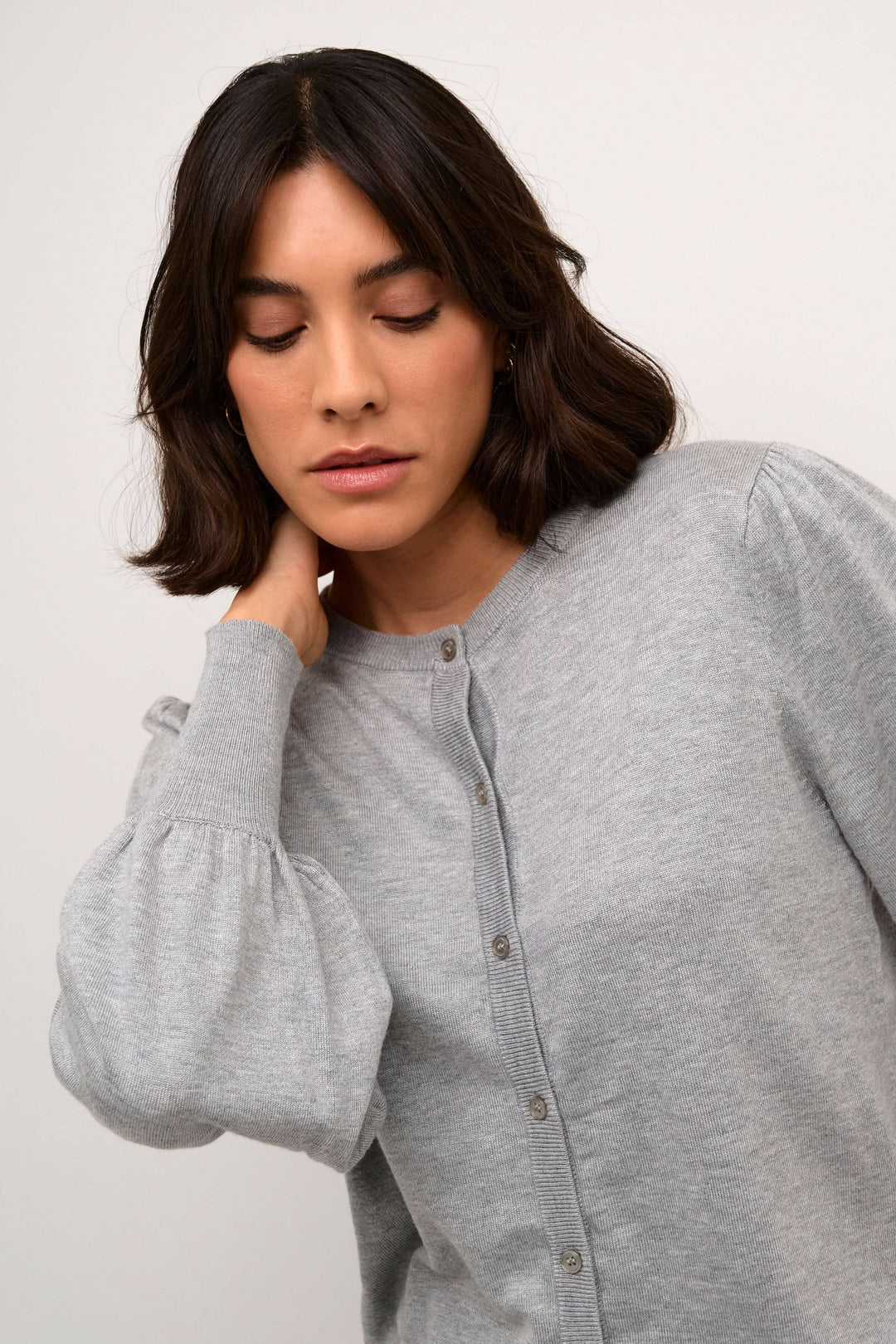 Femme portant un cardigan gris à manches ballons avec col rond et fermeture boutonnée.