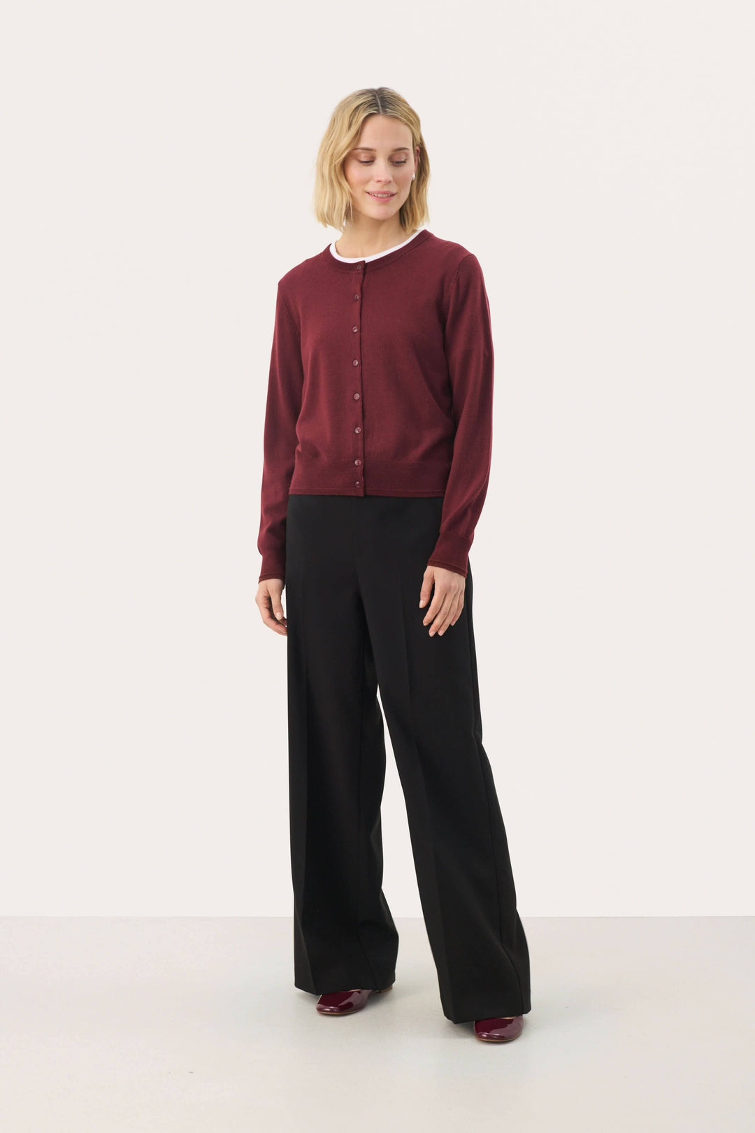 Cardigan Noelani classique à encolure ronde, porté avec un pantalon noir, idéal pour un look de bureau ou décontracté.