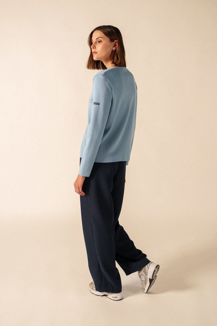 Femme portant un Cardigan de laine BREVANDS bleu, style minimaliste et intemporel, avec un pantalon bleu foncé et des baskets blanches.
