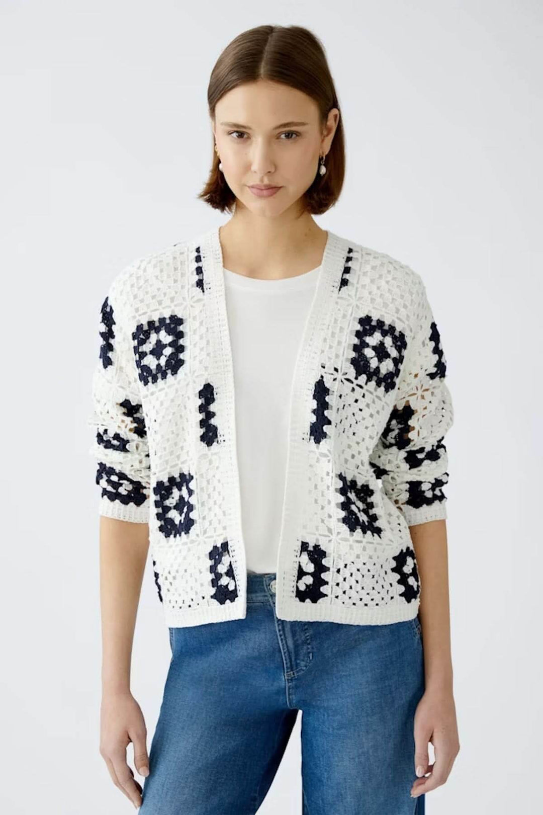 Cardigan en crochet blanc avec motifs géométriques marines, porté sur un t-shirt blanc et un jean bleu.