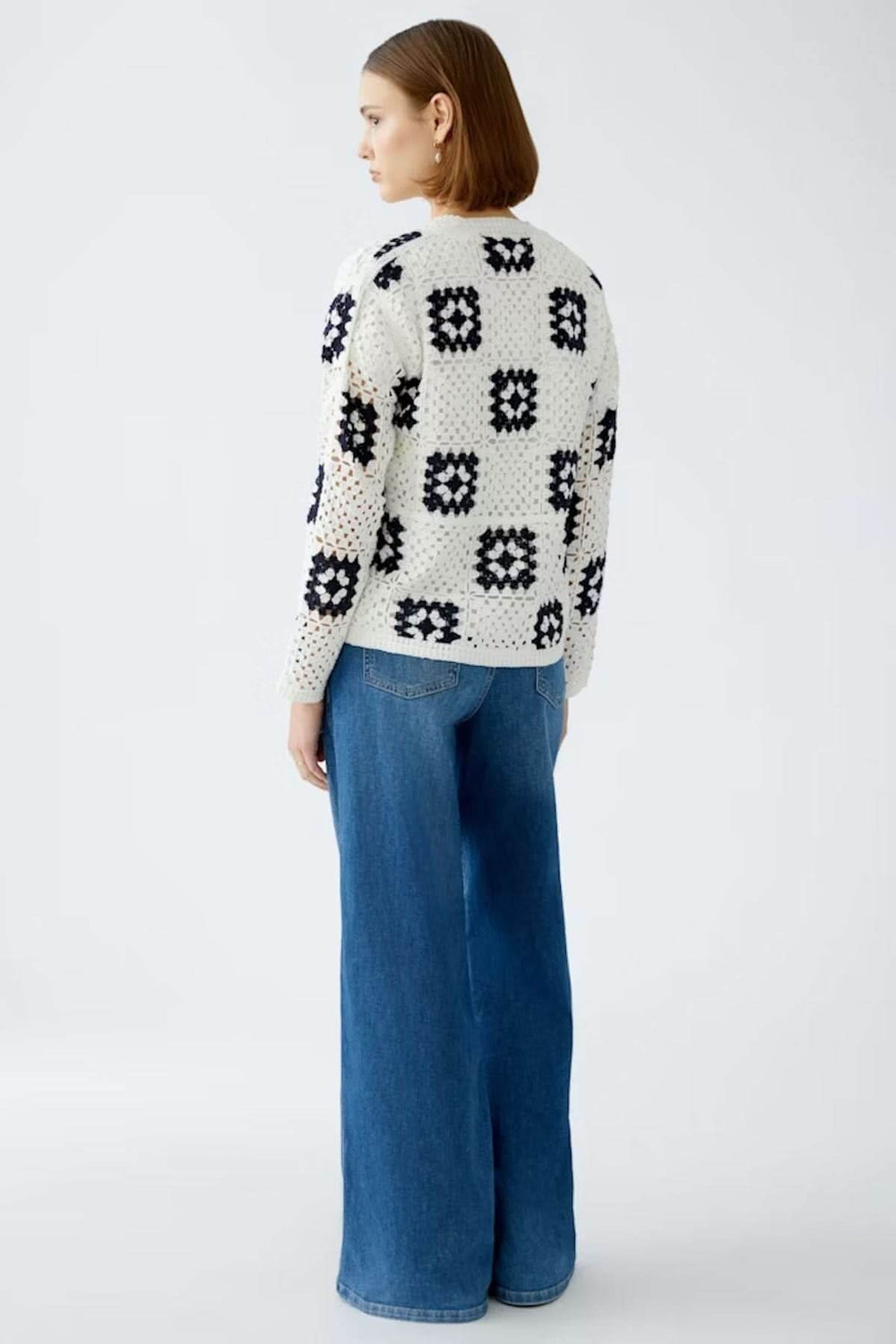 Cardigan en crochet blanc avec motifs géométriques, porté sur un jean bleu, pour un look bohème élégant.