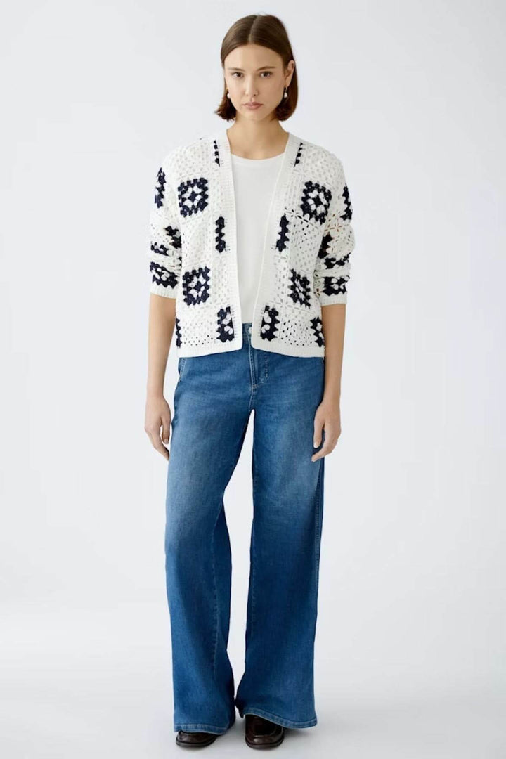 Cardigan en crochet blanc à motifs géométriques marines, porté avec un t-shirt blanc et un jeans bleu.