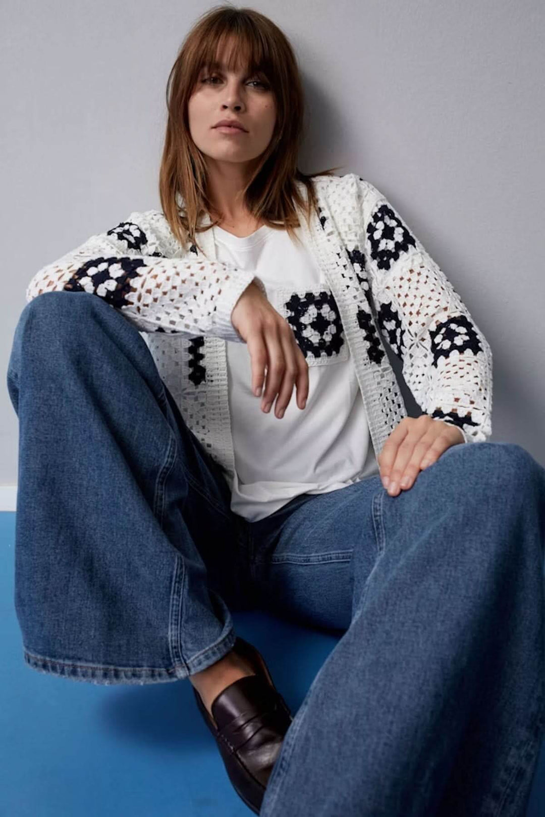 Cardigan en crochet blanc à motifs géométriques, porté avec un t-shirt blanc et un jean bleu, style bohème.