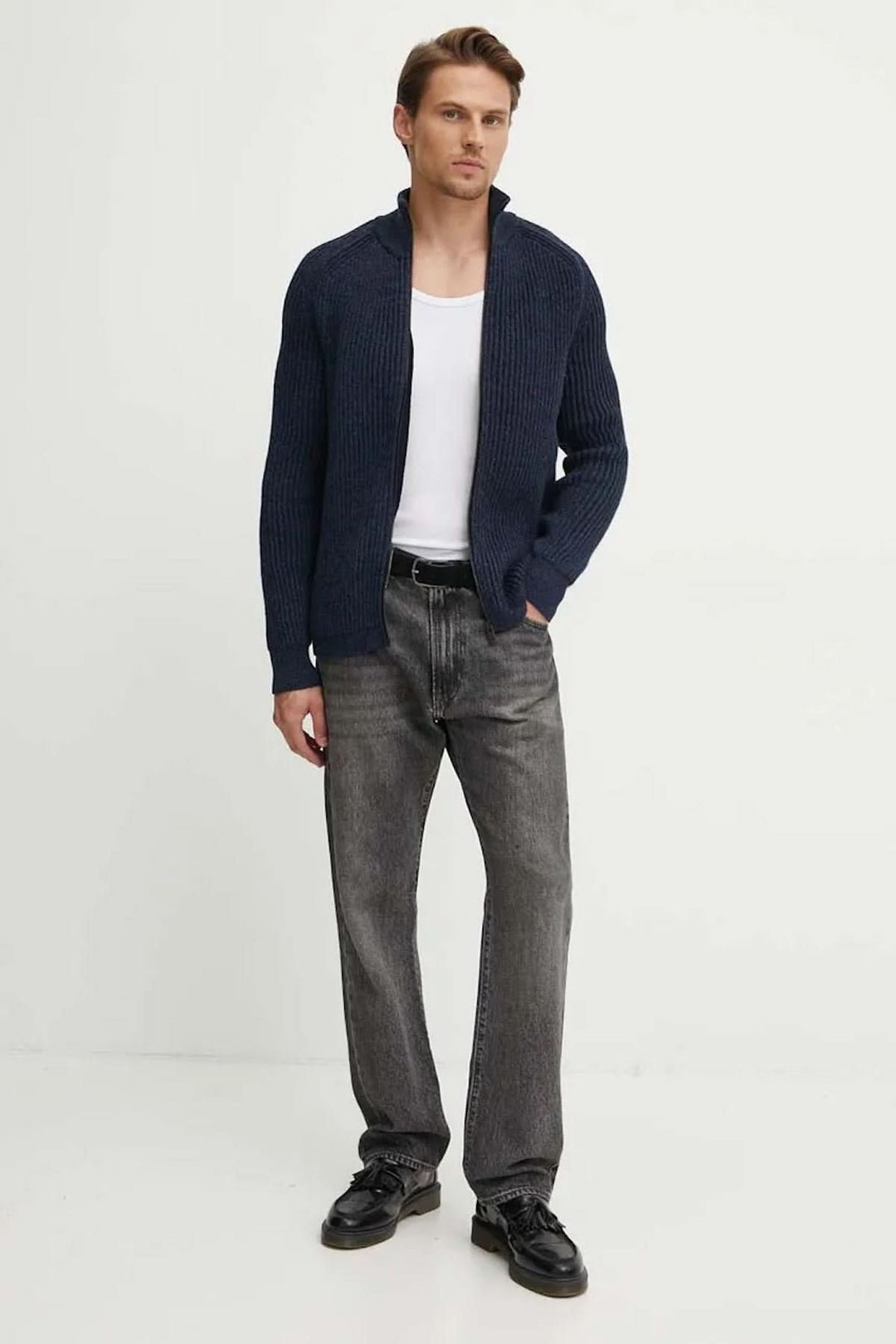 Homme portant un cardigan en laine bleu marine avec un col relevé, associé à un débardeur blanc et un pantalon gris.