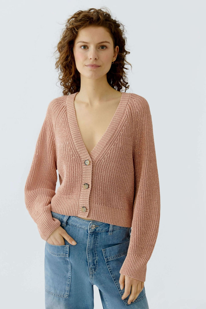 Cardigan tricoté rose à manches longues avec encolure en V, porté par-dessus un jean, pour un look élégant et décontracté.