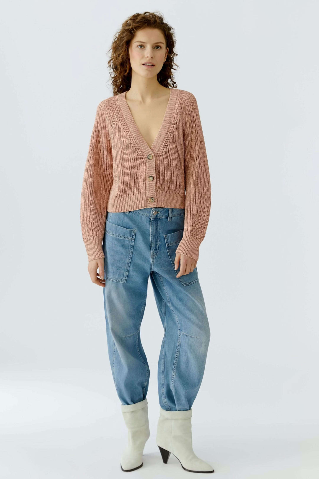 Femme portant un cardigan tricoté rose à encolure en V et boutons sur un jean décontracté.