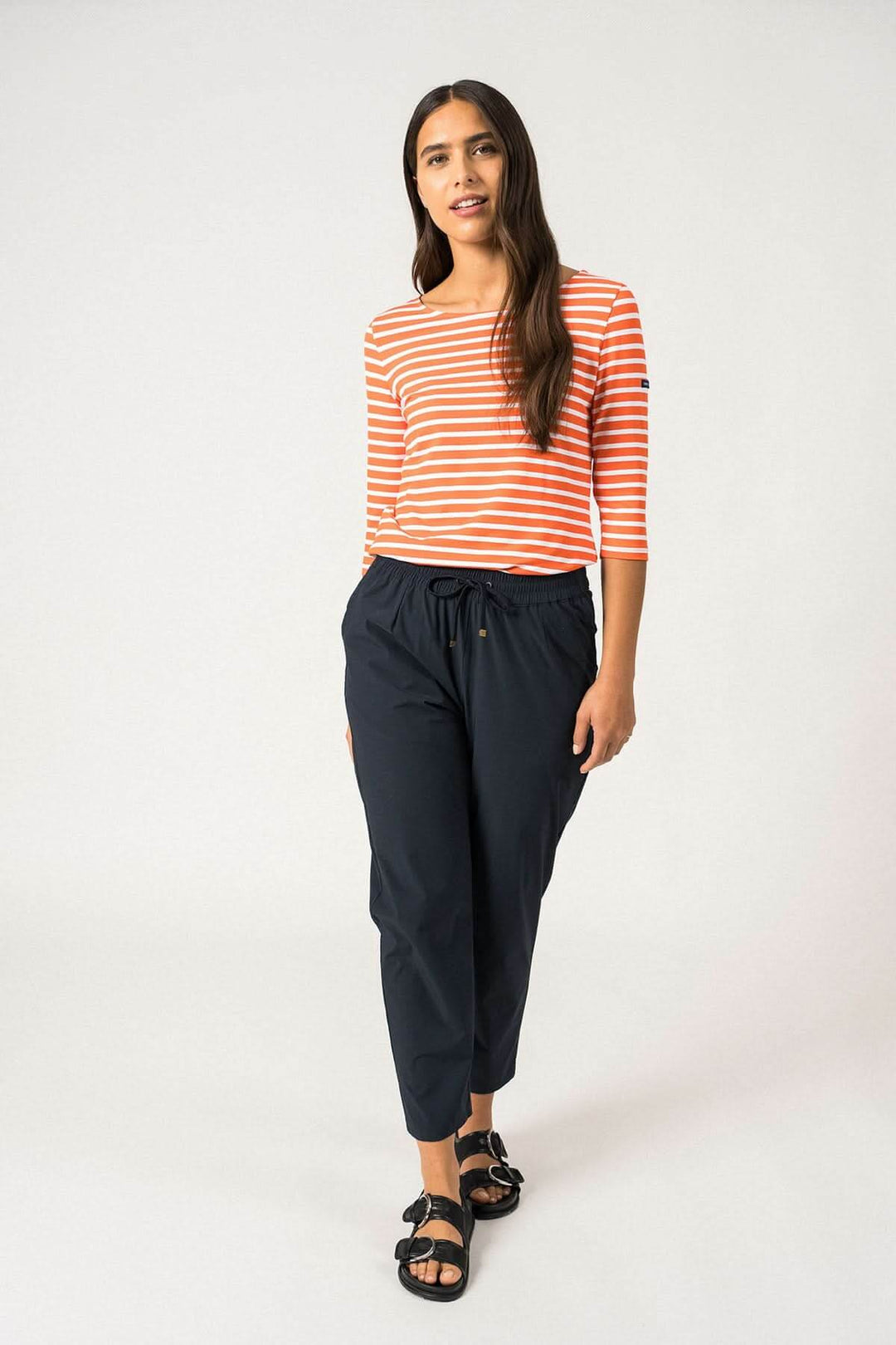 Femme portant un chandail rayé orange et blanc avec un pantalon noir, style décontracté et moderne.