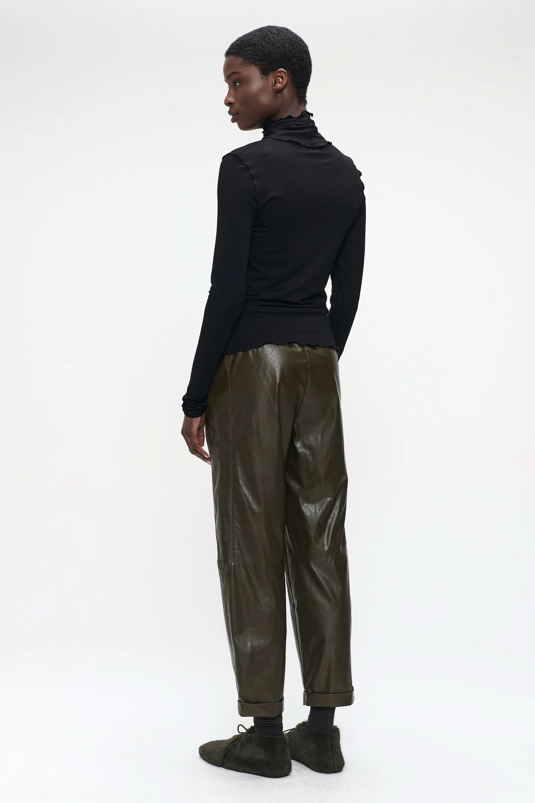 Person wearing Chandail Janice, black turtleneck sweater, styled with olive pants for a minimalistic and chic look.