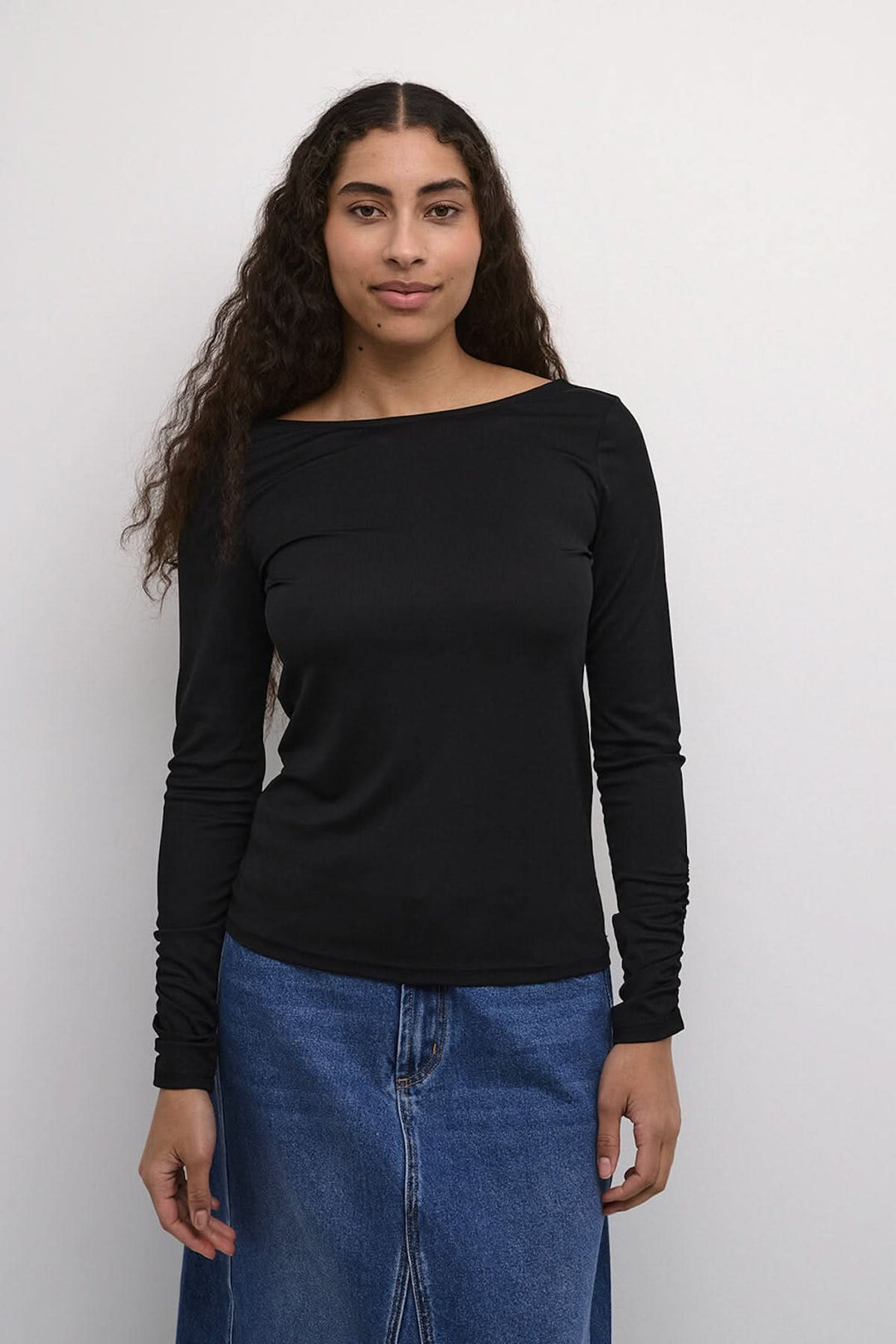Chandail noir Kaffe à manches longues, élégant avec dos dégagé, porté avec jupe en denim.