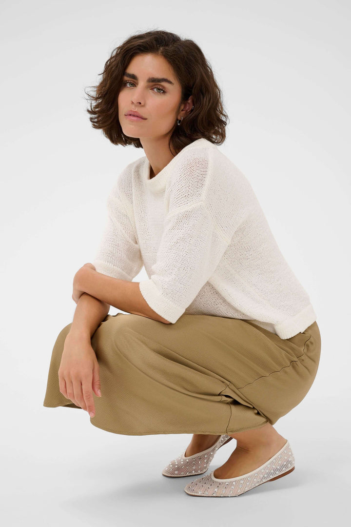 Femme portant le Chandail Sevita blanc en maille légère avec jupe kaki, style moderne et épuré.