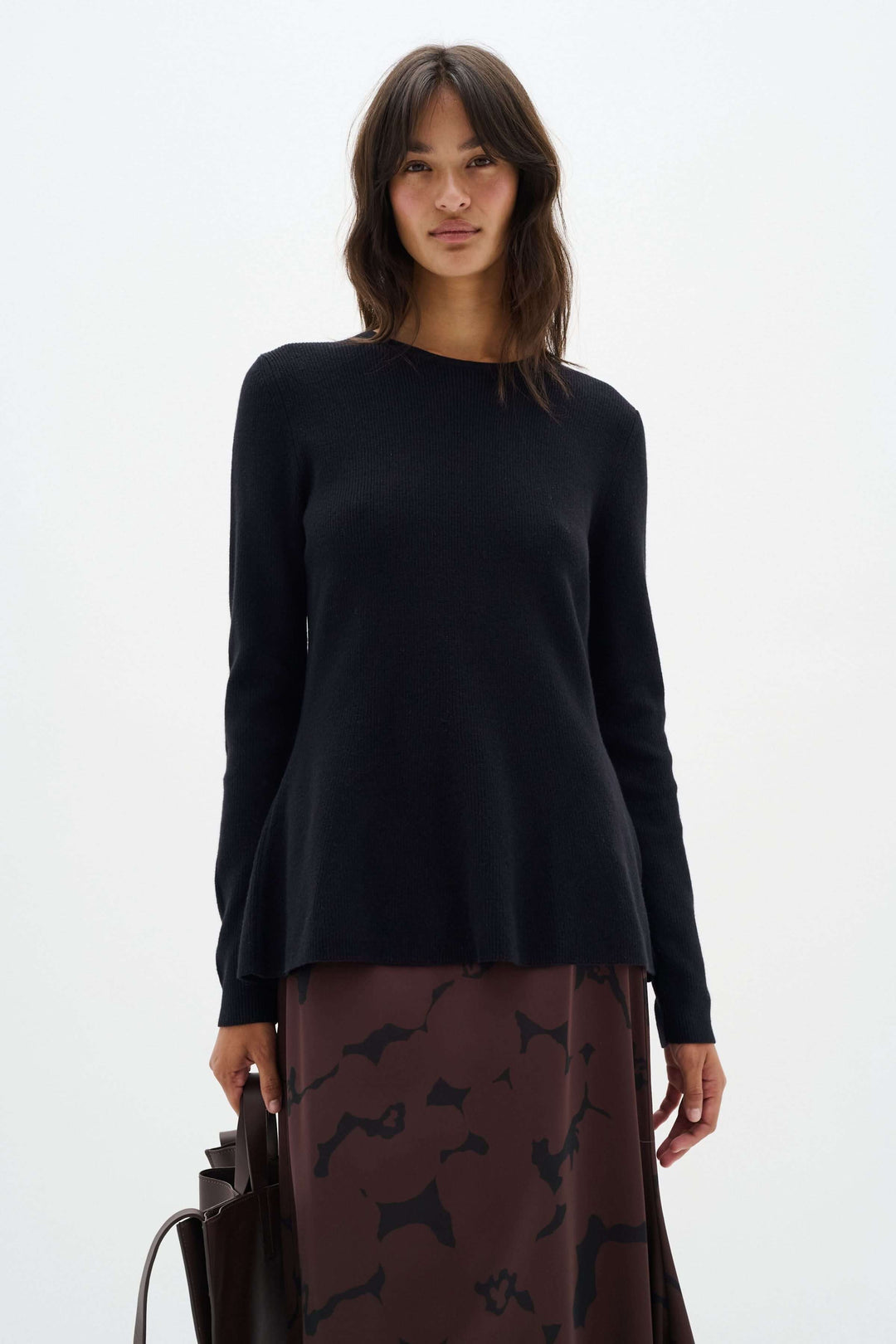 Chandail noir à col montant avec coupe péplum, porté par un mannequin, stylé avec une jupe marron.