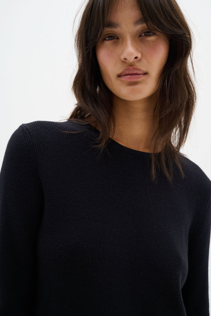 Chandail noir à col montant, coupe péplum, élégant et féminin, modèle portant taille 36/S.