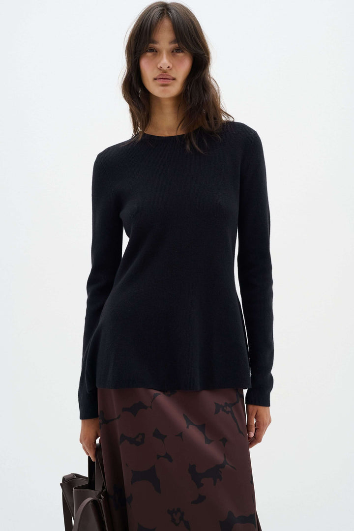 Chandail noir à col montant avec coupe péplum, porté avec une jupe brune, pour un look élégant.