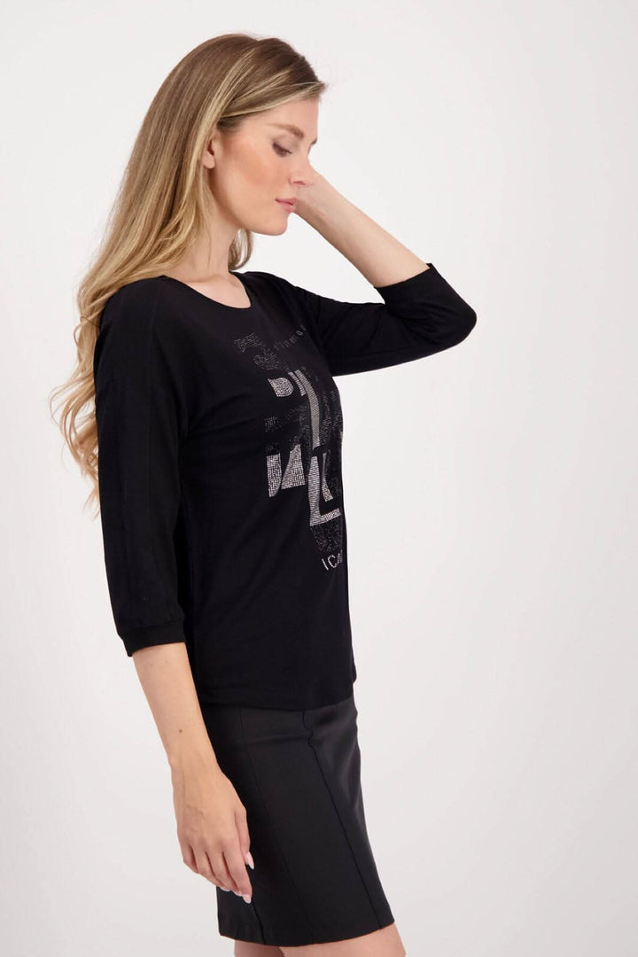 Femme portant un chandail noir Monari à lettrage décoratif en strass et manches 3/4, style décontracté.