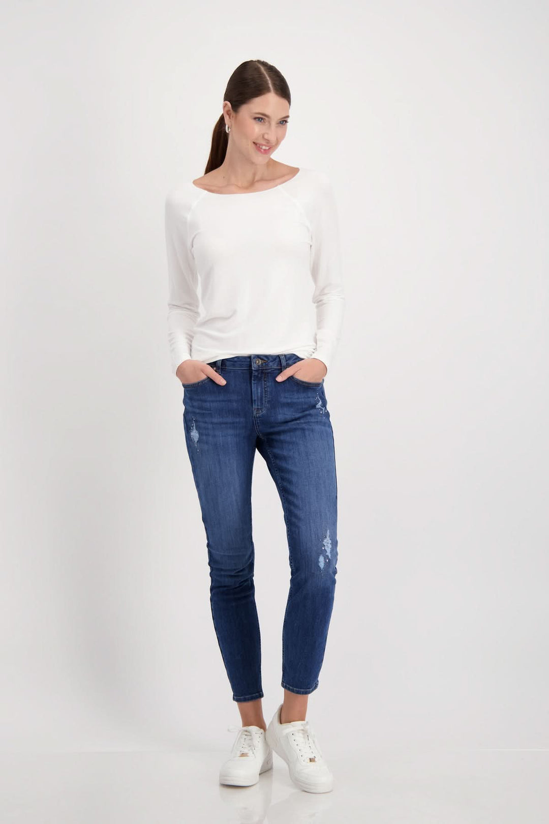 Femme souriante portant un chandail basique blanc et un jean bleu, style moderne et décontracté.