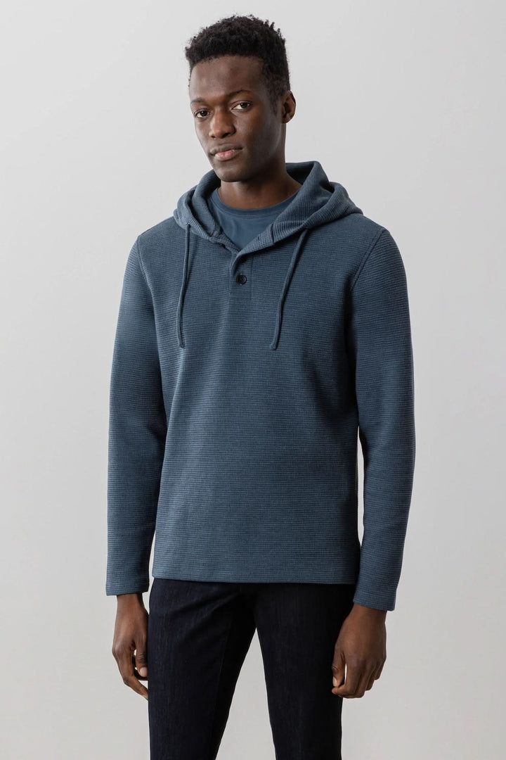 Homme portant un chandail capuchon bleu en tricot gaufré, idéal pour un style décontracté et confortable.