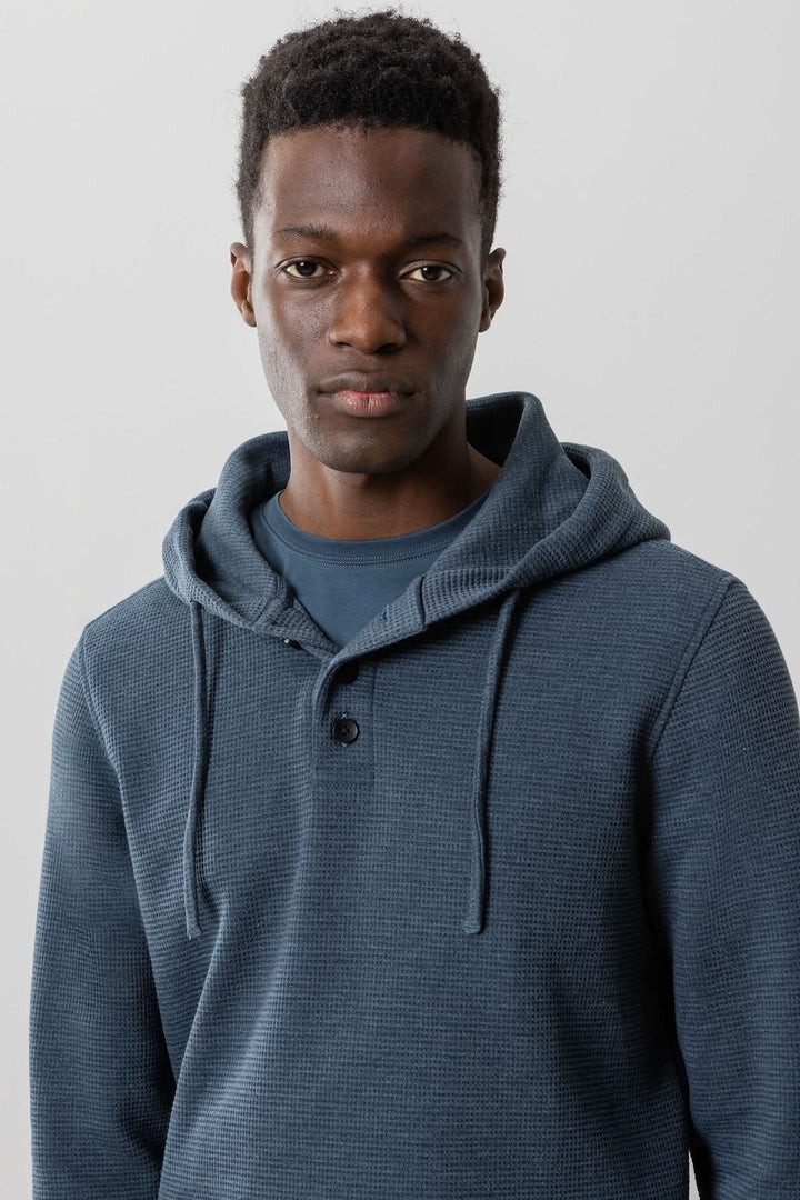 Homme portant un sweat à capuche Grenfell, en tricot gaufré texturé, couleur bleu, style décontracté.