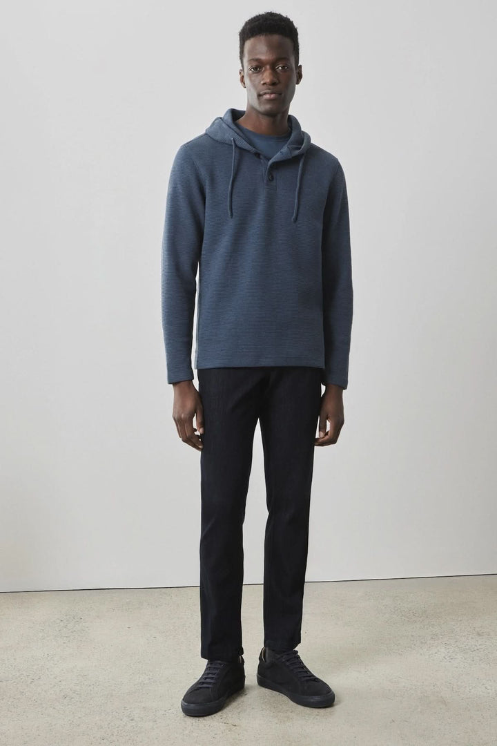 Homme portant un chandail capuchon bleu marine avec cordons, pantalon noir et chaussures décontractées.