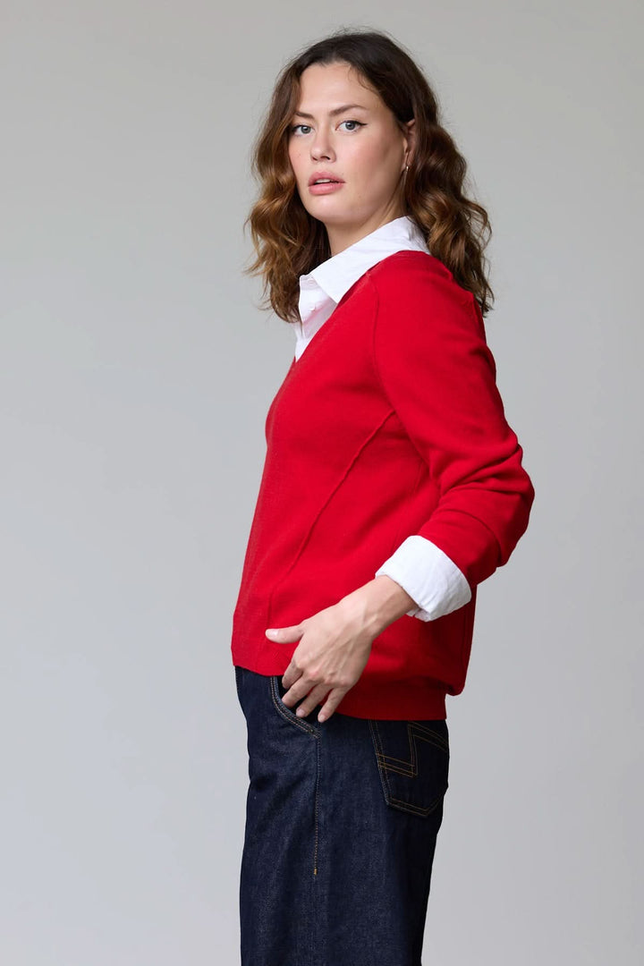 Femme portant un chandail col en V classique rouge avec chemise blanche en dessous, style élégant et polyvalent.