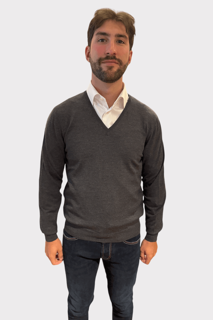 Homme portant un chandail gris col en V en laine au-dessus d'une chemise blanche, style élégant et confortable.