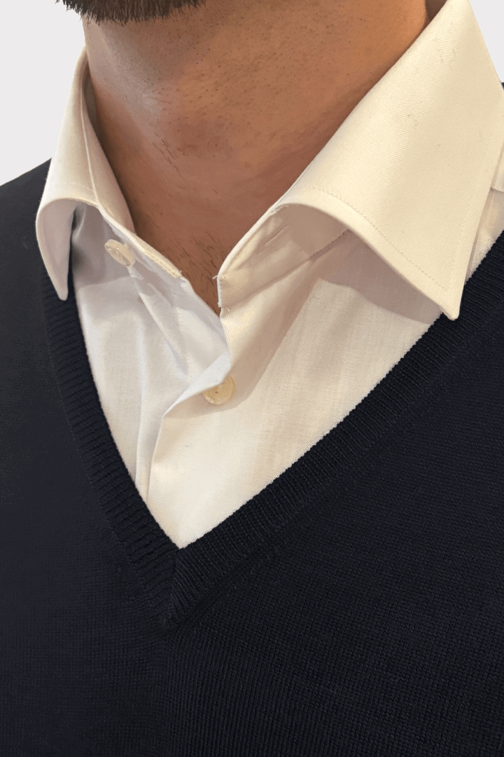 Chandail col en V en laine noir porté sur une chemise blanche, combinant confort et élégance.