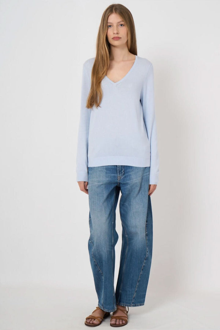 Femme portant un chandail col en V manches longues, couleur bleue, avec un jean. Style décontracté et élégant.