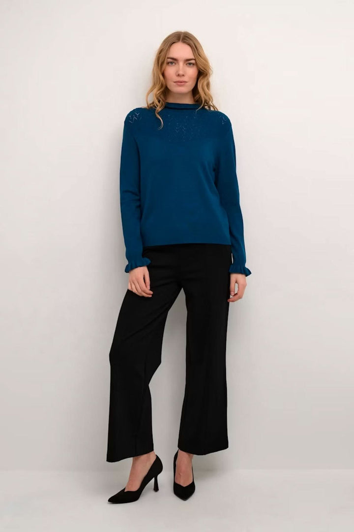 Femme portant un chandail à col montant bleu avec détails ajourés aux épaules, idéal pour un look chic et moderne.