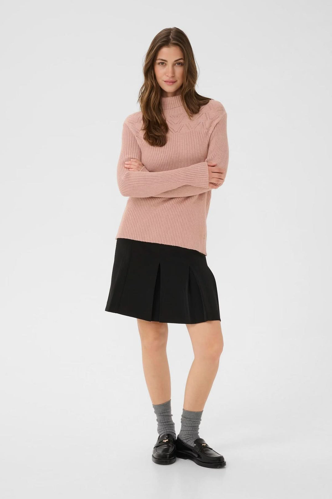 Femme portant un chandail à col montant rose avec une jupe noire, illustrant un style moderne et raffiné.