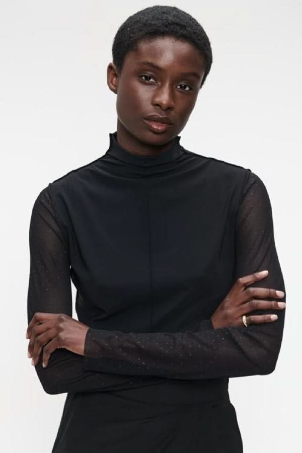 Femme portant un chandail à col montant et manches transparentes, coupe ajustée et élégante, idéal pour un look chic et sophistiqué.