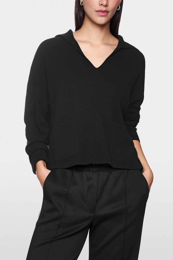 Chandail col ouvert noir avec manches longues et poches plaquées, porté pour un style décontracté élégant.