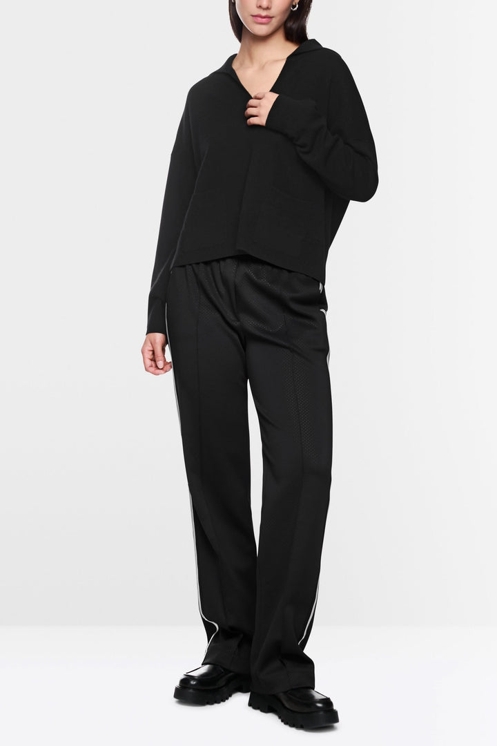 Femme portant un chandail col ouvert noir avec pantalon fluide, look décontracté et moderne.