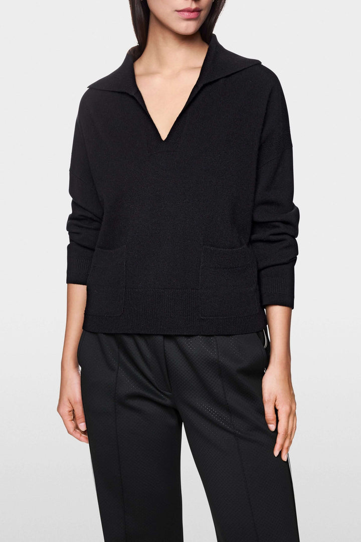 Femme portant un chandail col ouvert noir avec manches longues et poches plaquées, style décontracté et moderne.