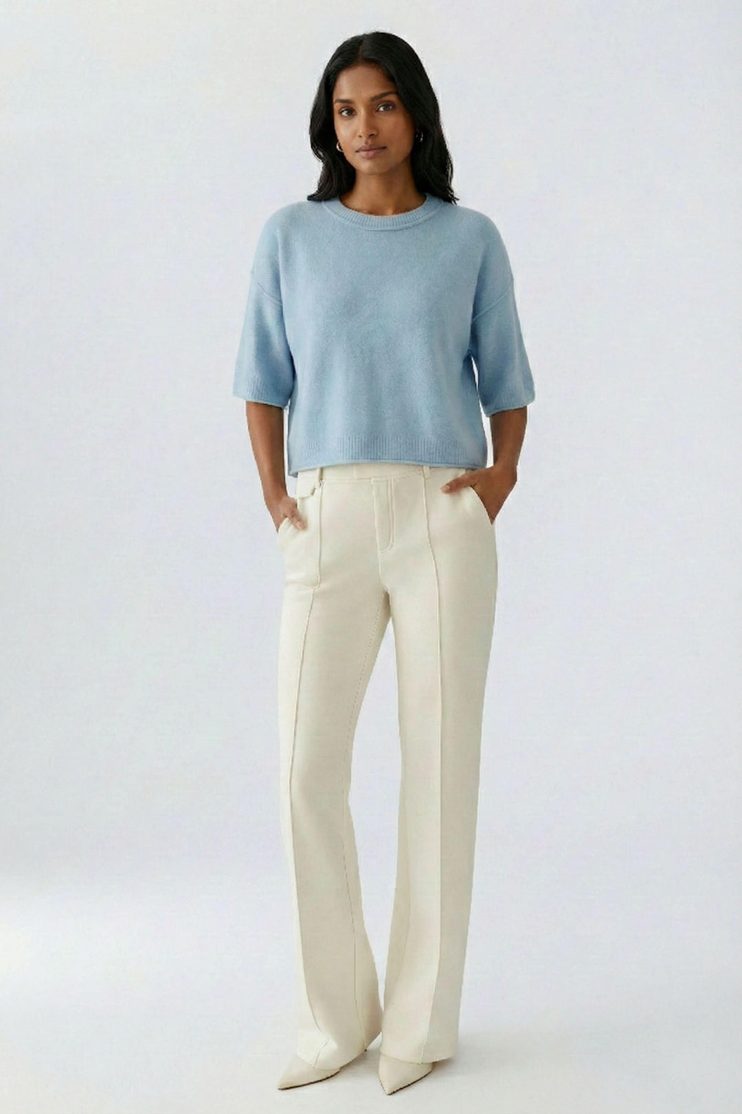 Femme portant un chandail court en maille douce à manches larges bleu avec un pantalon blanc, affichant un style moderne et décontracté chic.