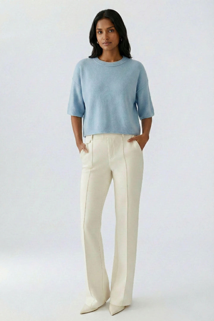 Femme portant un chandail court en maille douce à manches larges bleu avec un pantalon blanc, affichant un style moderne et décontracté chic.