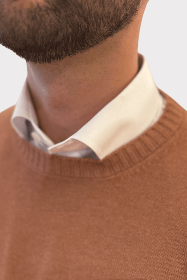 Gros plan sur un homme portant un pull en laine et cachemire orange avec un col blanc clair.
