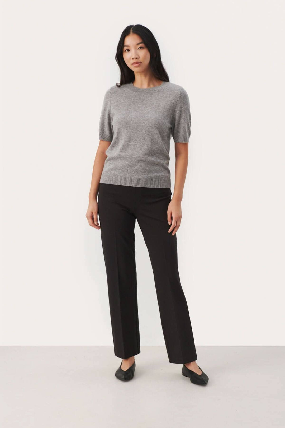 Chandail en cachemire gris à manches courtes, porté avec un pantalon noir élégant.