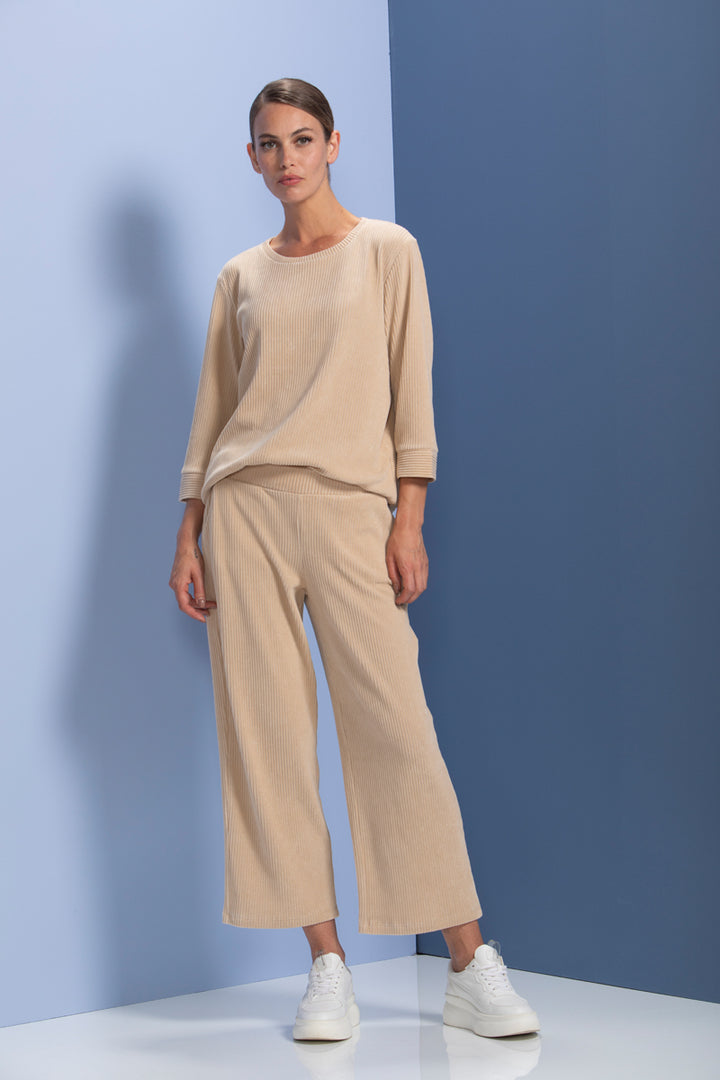 Femme portant un chandail en maille côtelée beige, coupe ample, manches trois-quarts, avec pantalon assorti, style moderne et confortable.