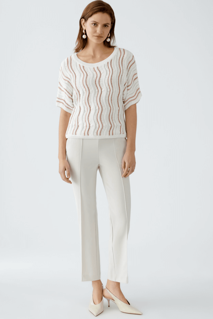 Femme portant un chandail en maille texturée avec motif ondulé et pantalon blanc, look décontracté et féminin.