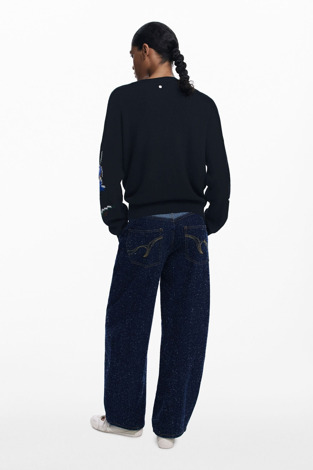 Homme portant un chandail à fleurs brodées et un jean ample, vue de dos, style décontracté.