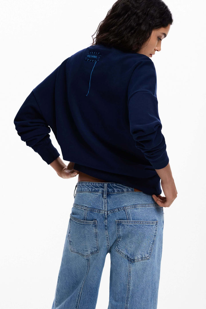 Femme portant un chandail à grande fleur bleu avec jeans, vue de dos.