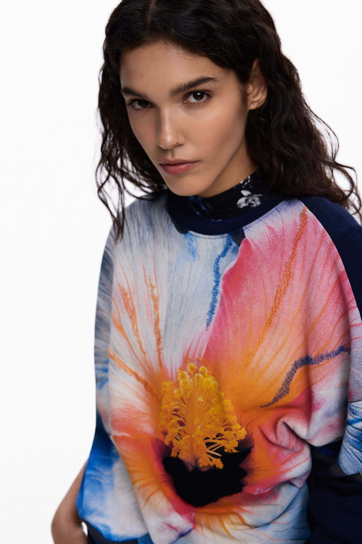 Femme portant un chandail à grande fleur avec motif floral surdimensionné, style moderne et expressif.