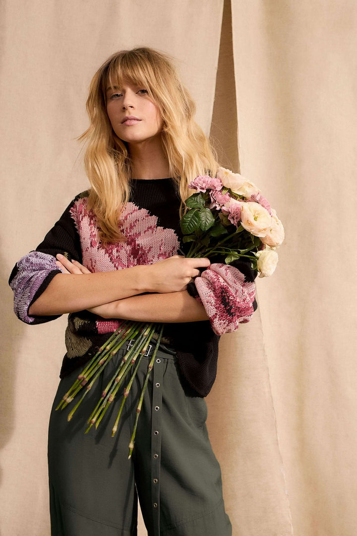 Femme portant un chandail imprimé floral avec détails ajourés, en tenue décontractée, tenant un bouquet de fleurs.