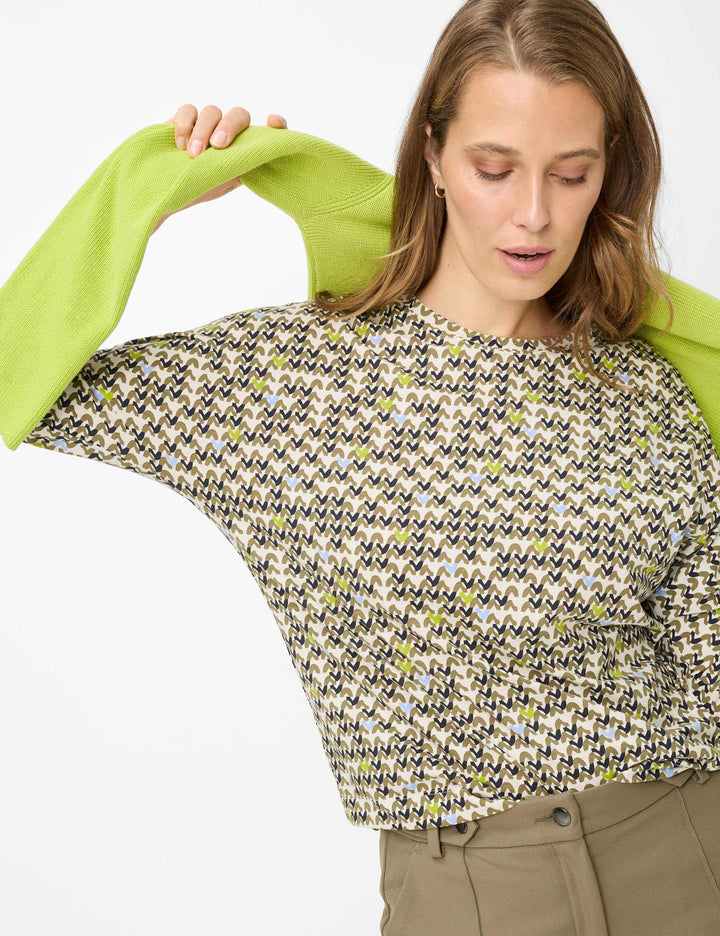 Femme portant le Chandail imprimé graphique CHARLENE avec motif dynamique et manches trois-quarts, ajoutant une touche contemporaine.