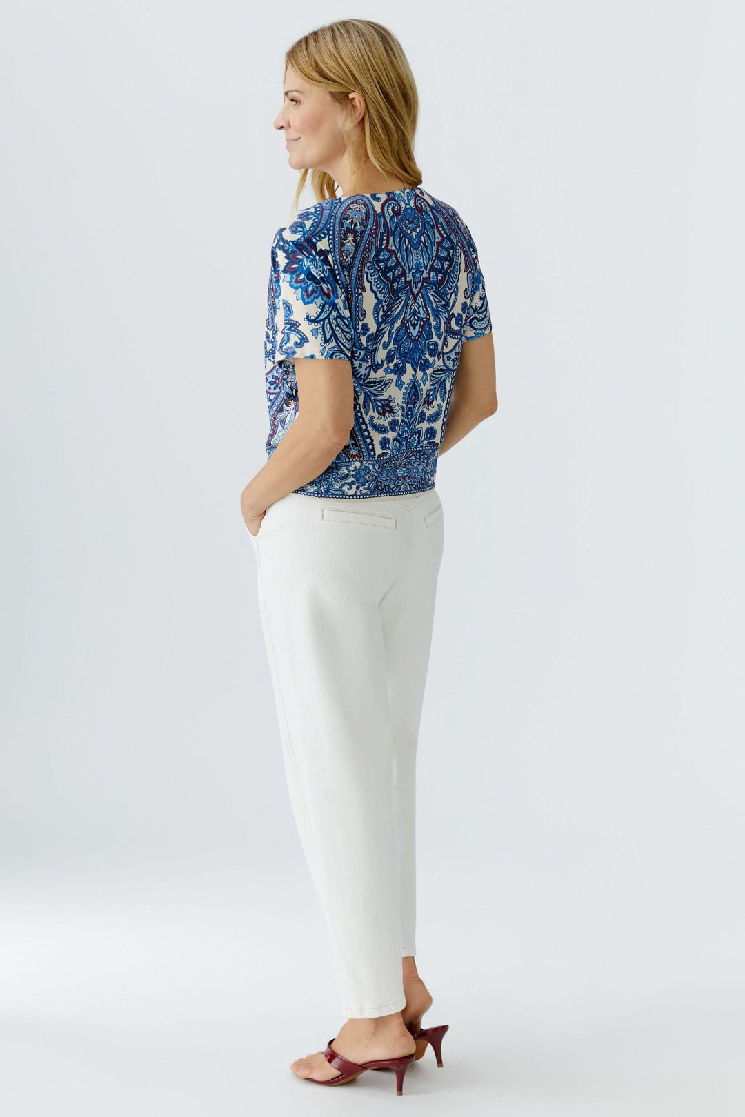 Femme portant un chandail imprimé à manches courtes avec motif cachemire élégant, assorti à un pantalon blanc pour un look chic.
