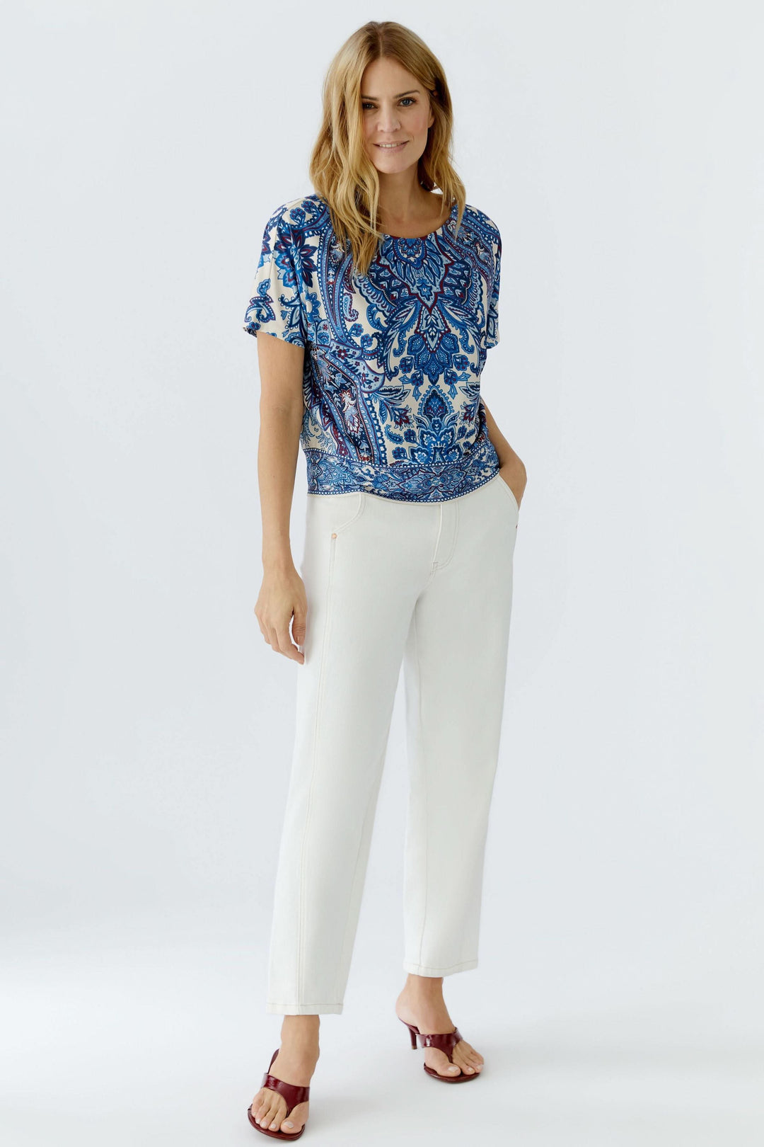 Chandail imprimé à manches courtes au motif cachemire, porté avec un pantalon blanc pour un look décontracté et raffiné.