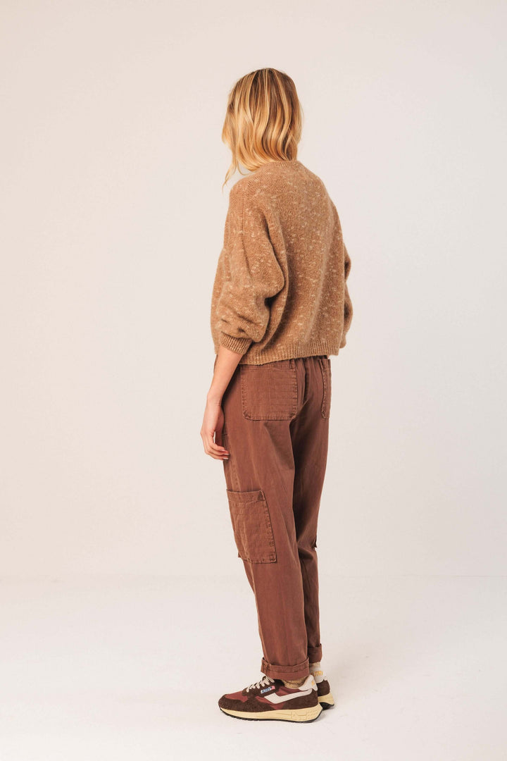 Femme portant un chandail maille texturée avec coupe décontractée, manches bouffantes, et col rond, associée à un pantalon marron.