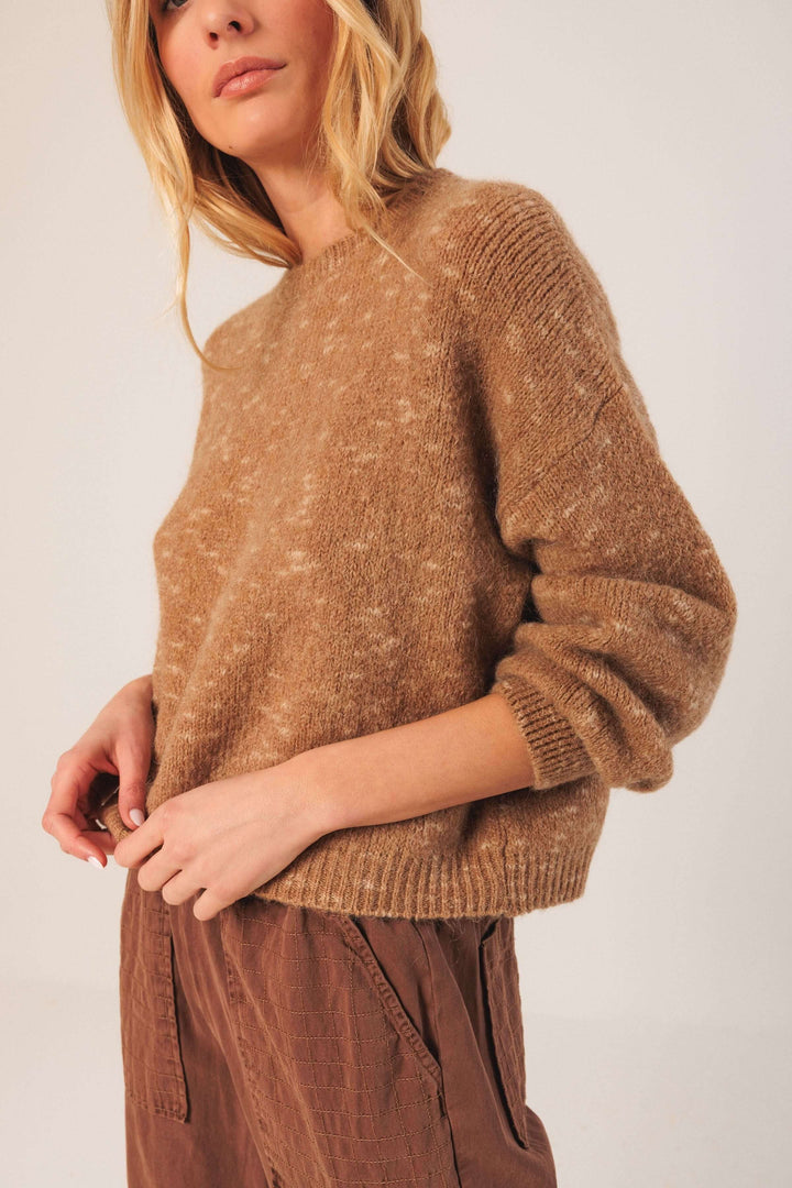 Femme portant un chandail maille texturée avec manches bouffantes, idéal pour un look décontracté et chaleureux en saison froide.