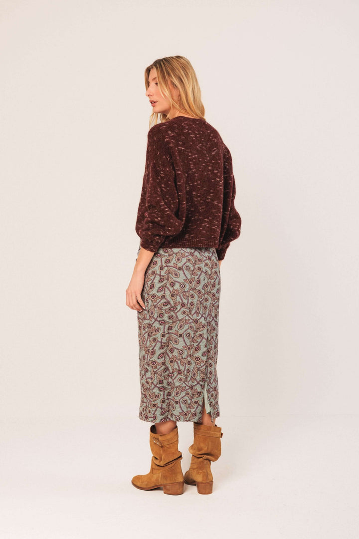 Chandail maille texturée avec col rond et manches bouffantes, porté avec une jupe imprimée pour un look tendance.