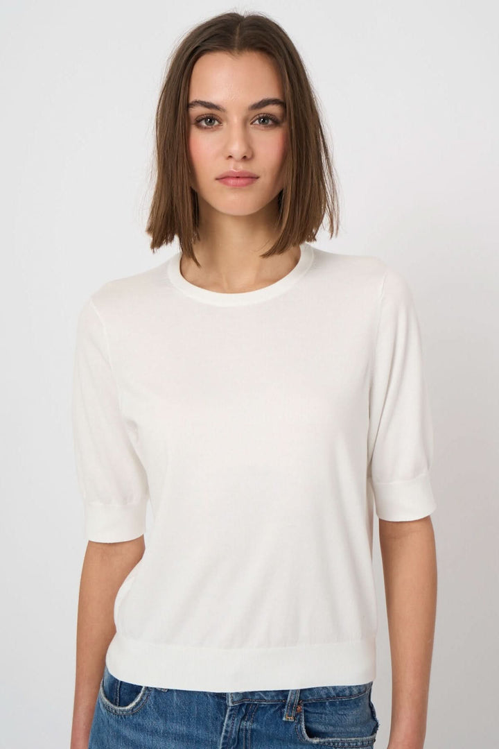 Femme portant un chandail à manches courtes blanc, coupe droite et confortable, avec une encolure ronde et manches ajustées.