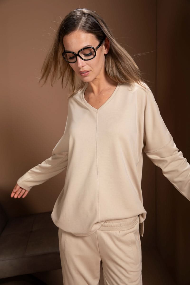 Femme portant un chandail minimaliste beige avec encolure en V et manches longues, coupe ample, décontracté et moderne.